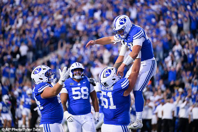 BYU offensive lineman Sonny Makasini, center right, lifts quarterback Bear Bachmeier, top, after Bachmeier ran for a touchdown during the first half of Saturday's upset win over the Irish