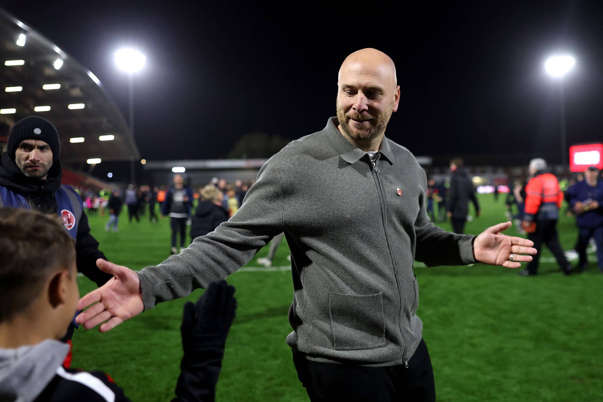 Ein Mann im grauen Pullover schüttelt nach einem Fußballspiel auf dem Spielfeld die Hand eines Fans.