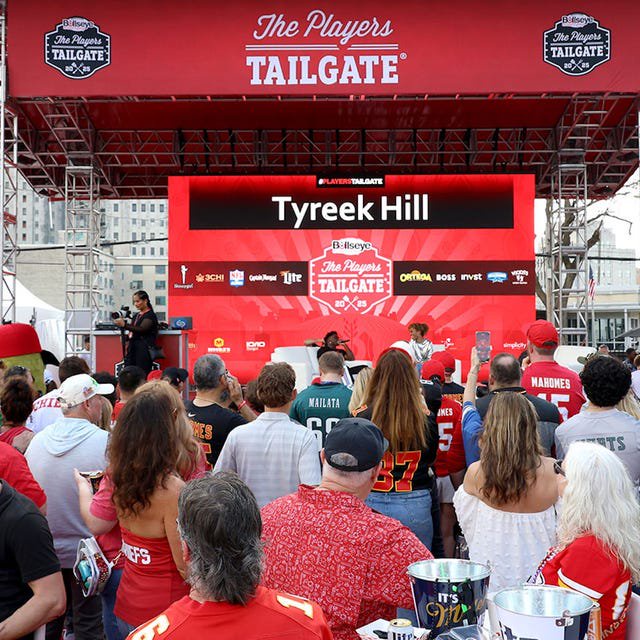 outdoor tailgate event with a crowd and a stage featuring a speaker