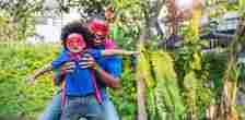 Father's Day - Happy black African American father daughter playing home outdoor. Afro man carry piggyback little toddler super hero boy. Cheerful family bonding together fatherâs day concept banner with copy space