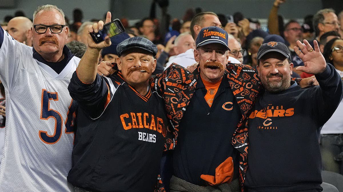 Fans wearing costume mustaches cheer in a stadium after a moment of silence honoring Mike Ditka.