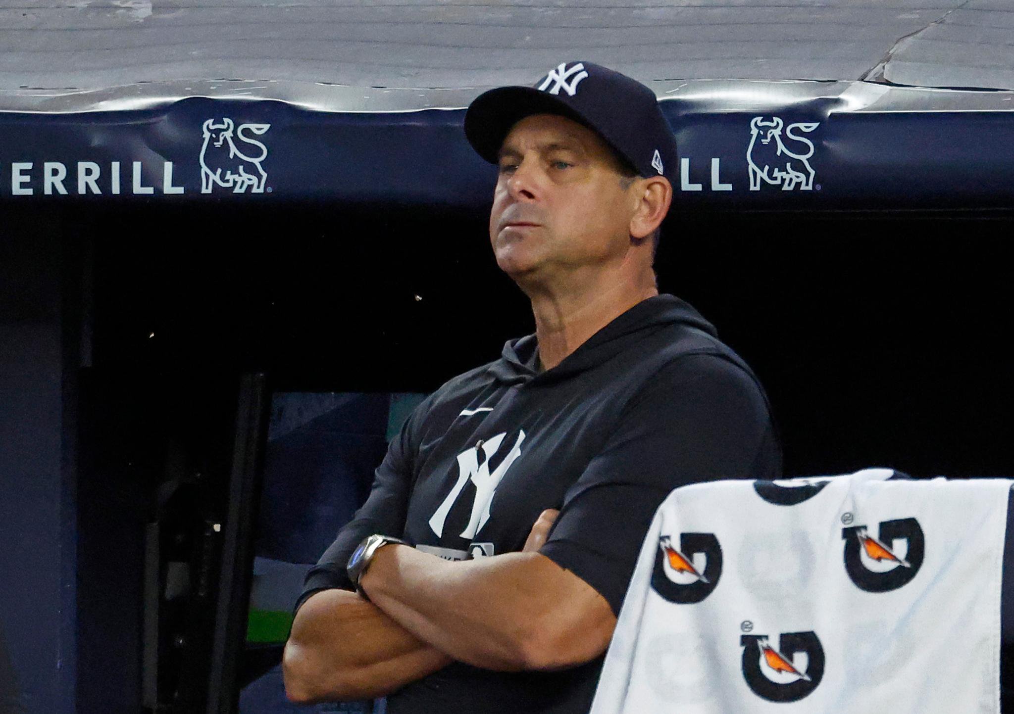 New York Yankees manager Aaron Boone stands in the dugout with his arms crossed.