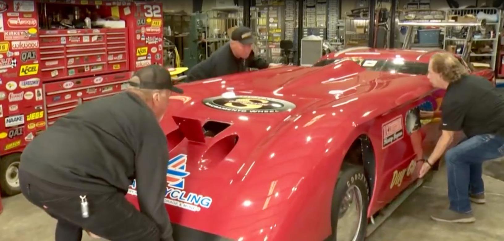 Gary Matranga and his team work on his red racing car in a garage.