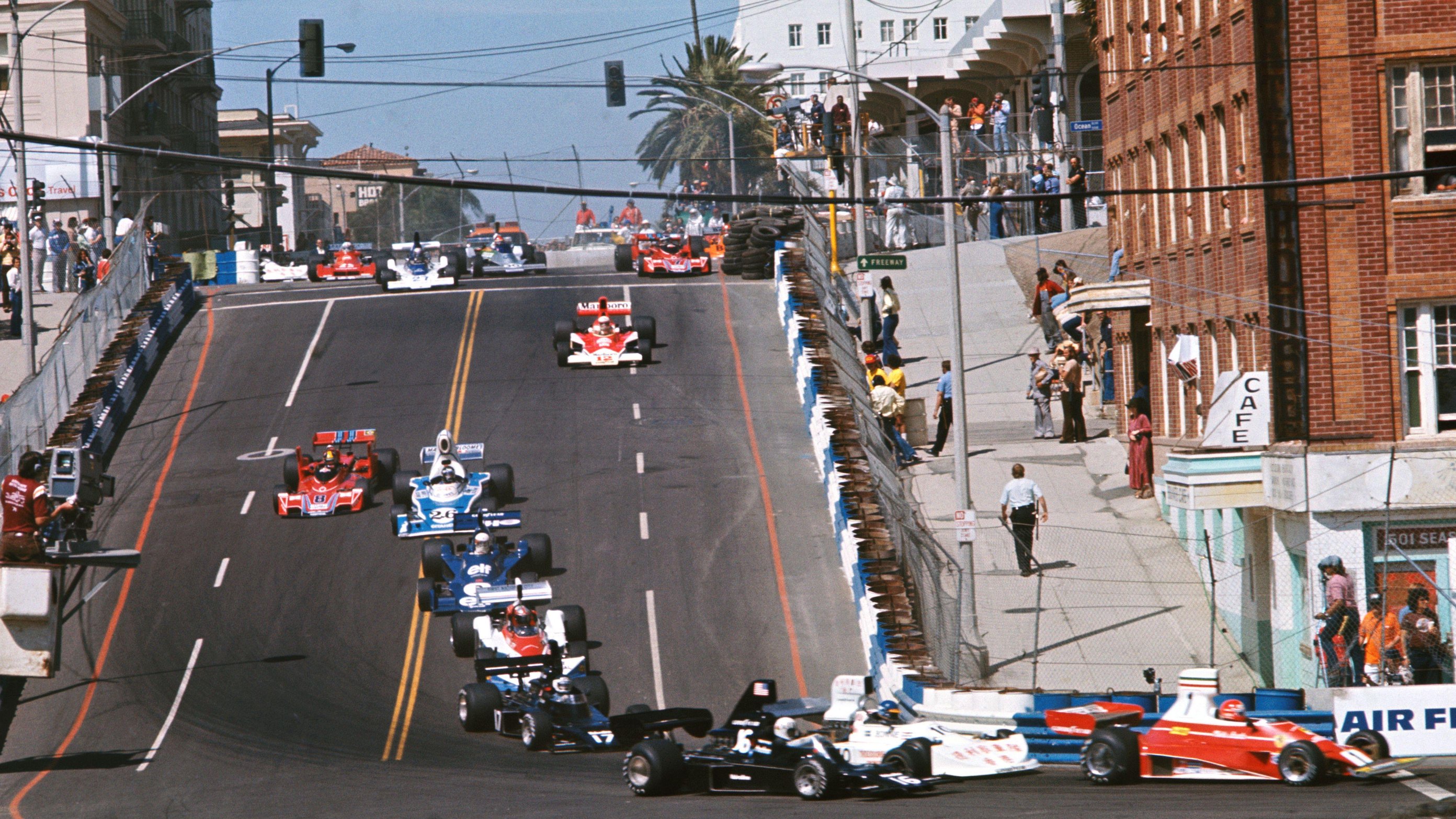 Formula 1 cars head down Linden Avenue during the 1976 United States Grand Prix West at Long Beach. Ferrari's Niki Lauda leads the pack while among those following him are Ronnie Peterson, Tom Pryce, Jean-Pierre Jarier, John Watson, Jody Scheckter, Jacques Laffite, Carlos Pace, Jochen Mass, Mario Andretti, Emerson Fittipaldi and Chris Amon