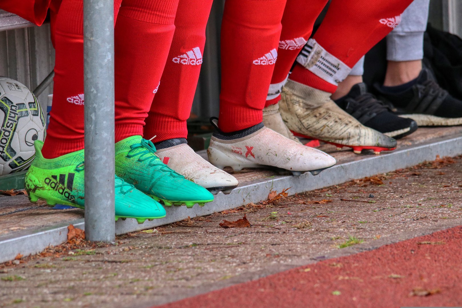 Fußballschuhe auf Ersatzbank, alle mit roten Stutzen