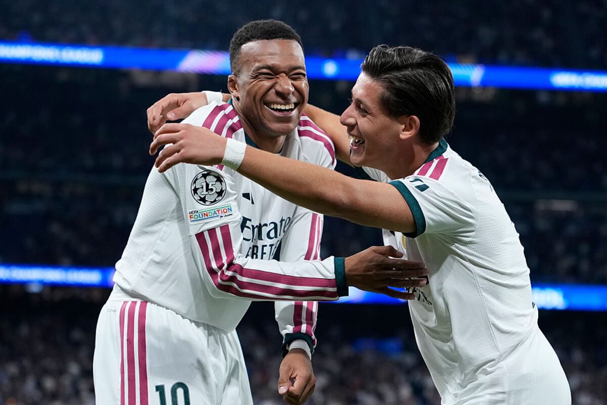 Kylian Mbappé in a white jersey with number 10, celebrating with a teammate on a soccer field.