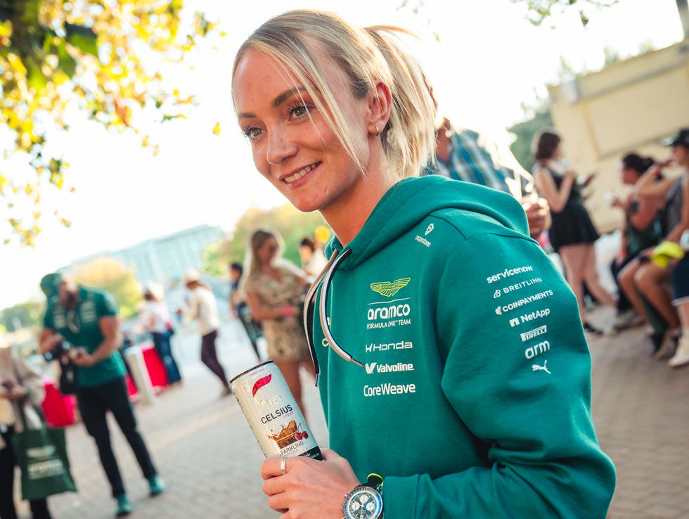 person in teal hoodie holding a can outdoors with crowd in background