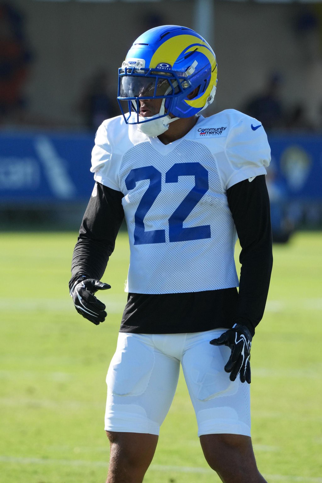 A football player in a blue and yellow helmet, white jersey with number 22, and white pants during Los Angeles Rams training camp.