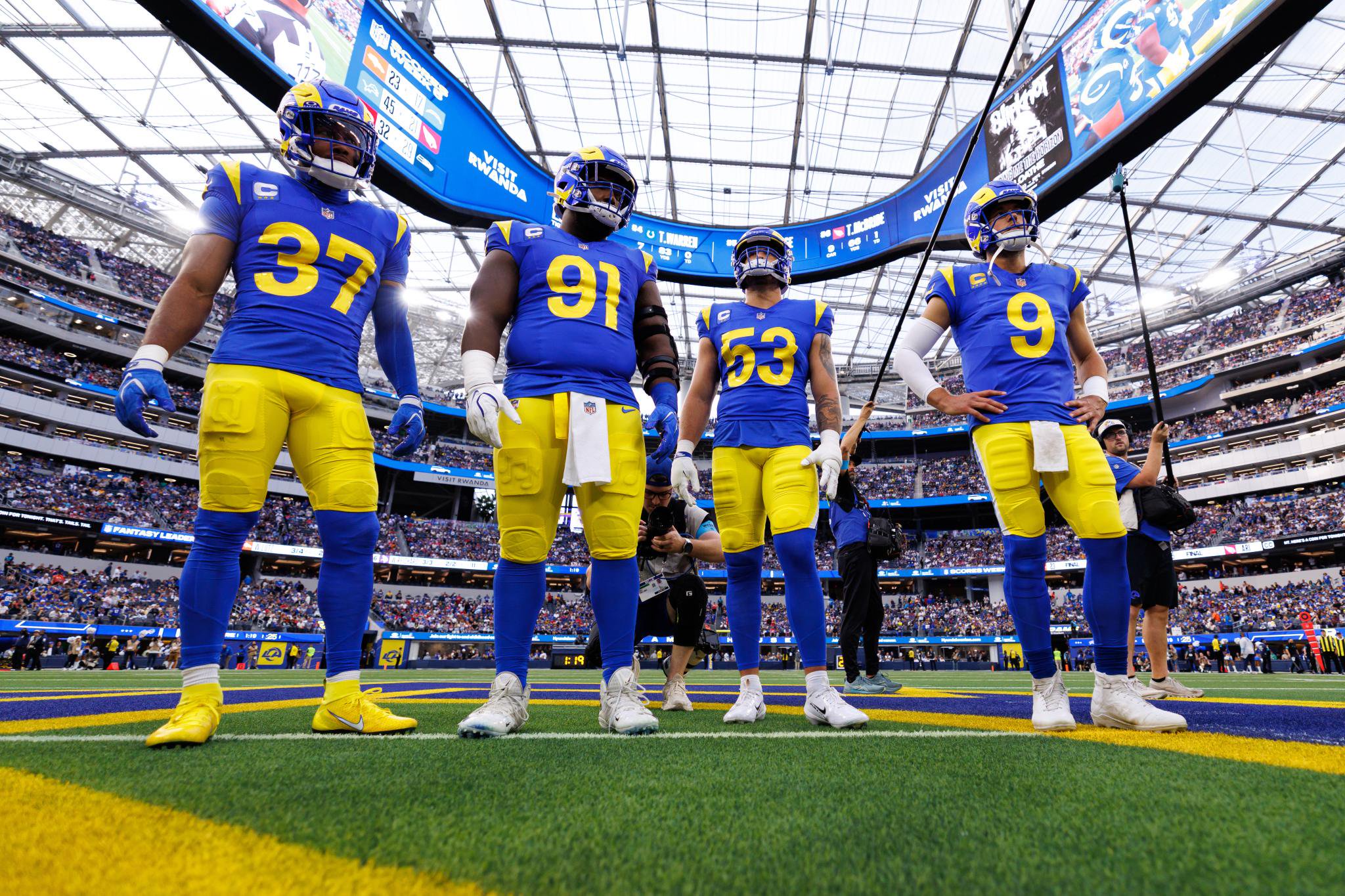 Four Los Angeles Rams football players in blue and yellow uniforms stand on the field, looking up during a game against the Buffalo Bills.