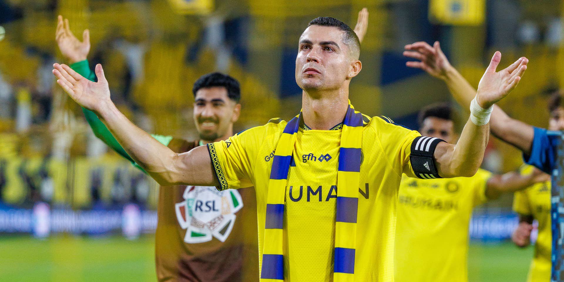 Cristiano Ronaldo breitet im gelben Trikot von Al-Nassr mit einem gelb-blauen Schal um den Hals jubelnd die Arme aus.
