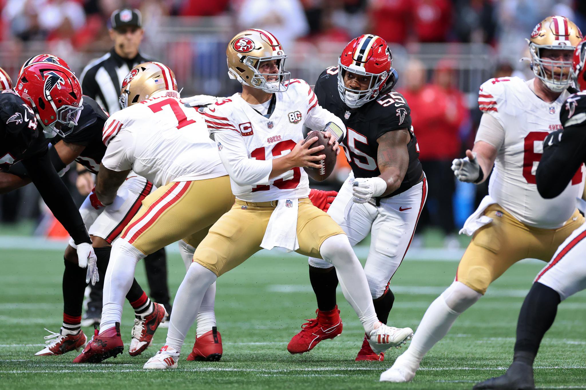 San Francisco 49ers quarterback Brock Purdy scrambles with the ball under pressure from Atlanta Falcons linebacker Za'Darius Smith.