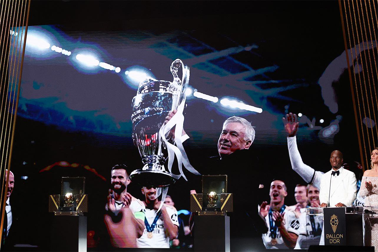Carlo Ancelotti on stage with the Champions League trophy at the Ballon d'Or ceremony, alongside other players and hosts.