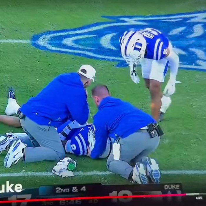 Football player receiving field treatment during game with staff kneeling beside him