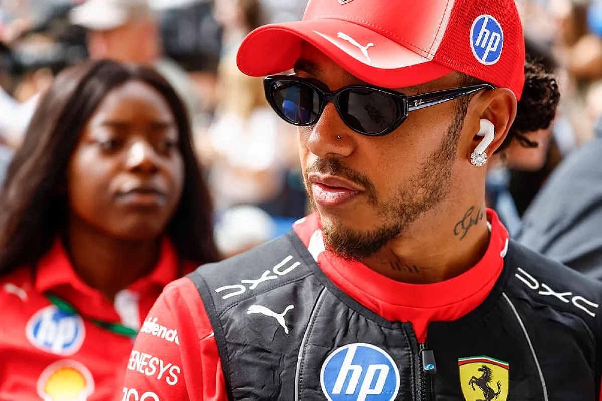 Driver in red Ferrari cap and black race jacket with HP and Puma logos at an F1 event; woman in red polo nearby.