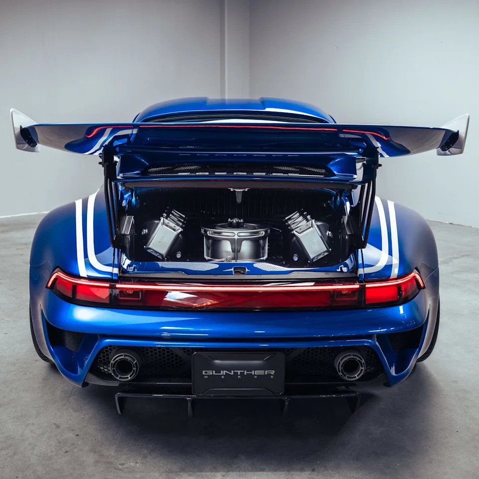 Blue sports car with a rear spoiler and open trunk displaying the engine and components.