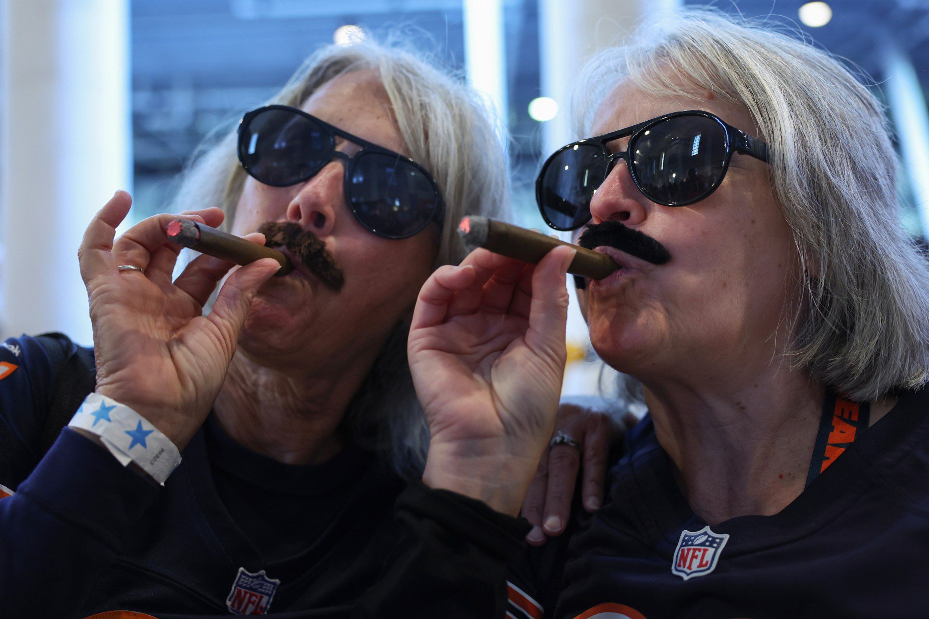 Nancy Davis, left, and Kathy Flint wear fake mustaches resembling former Bears head coach and player Mike Ditka, along with fake cigars, while taking pictures before a Bears-Patriots game at Soldier Field on Oct. 22, 2026. The two fans came with their own props even though fake mustaches were given to fans at the entry gates. (John J. Kim/Chicago Tribune)