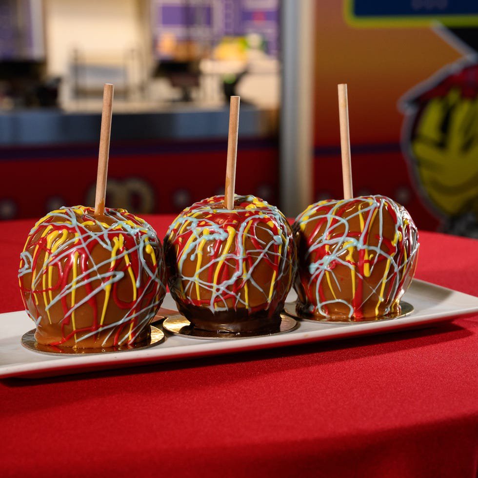 Three caramel apples with colorful drizzles on a white platter.