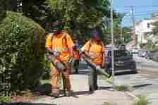 City workers with the Office of Clean and Green blow debris from a sidewalk in West Philadelphia as part of the city's 13-week summer cleaning program. The program is a pillar of Mayor Cherelle L. Parker's first year in office.