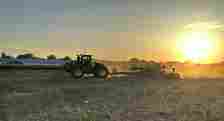 A John Deere tractor pulls a green and yellow planter through a South Dakota field at sunset