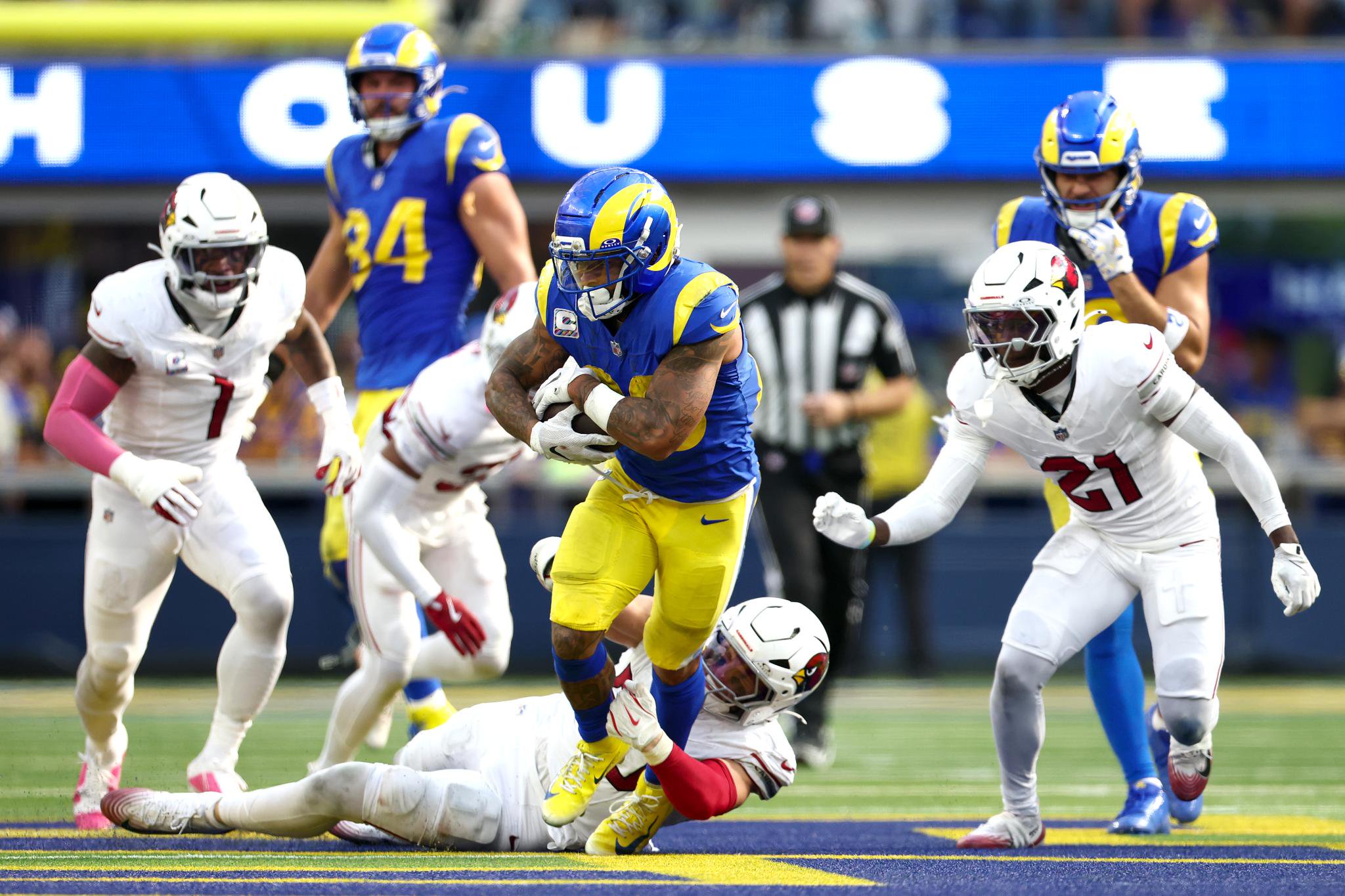 Los Angeles Rams running back carries the ball while being tackled by Arizona Cardinals defenders during a game.