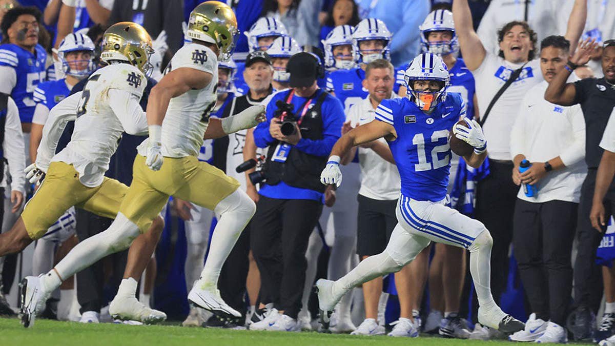 Preston Rex runs with the ball as Leonard Moore and Luke Talich chase him during a college football game.
