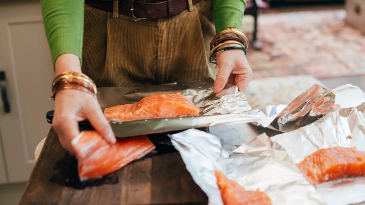 woman wrapping salmon in tin foil on kitchen worktop