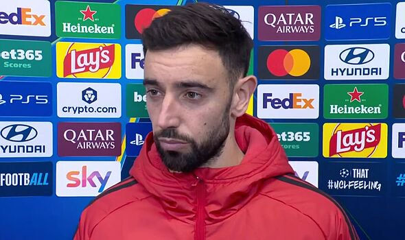 An individual, dressed in a red jacket and with a beard, is engaged in an interview. He is positioned before a microphone, with 