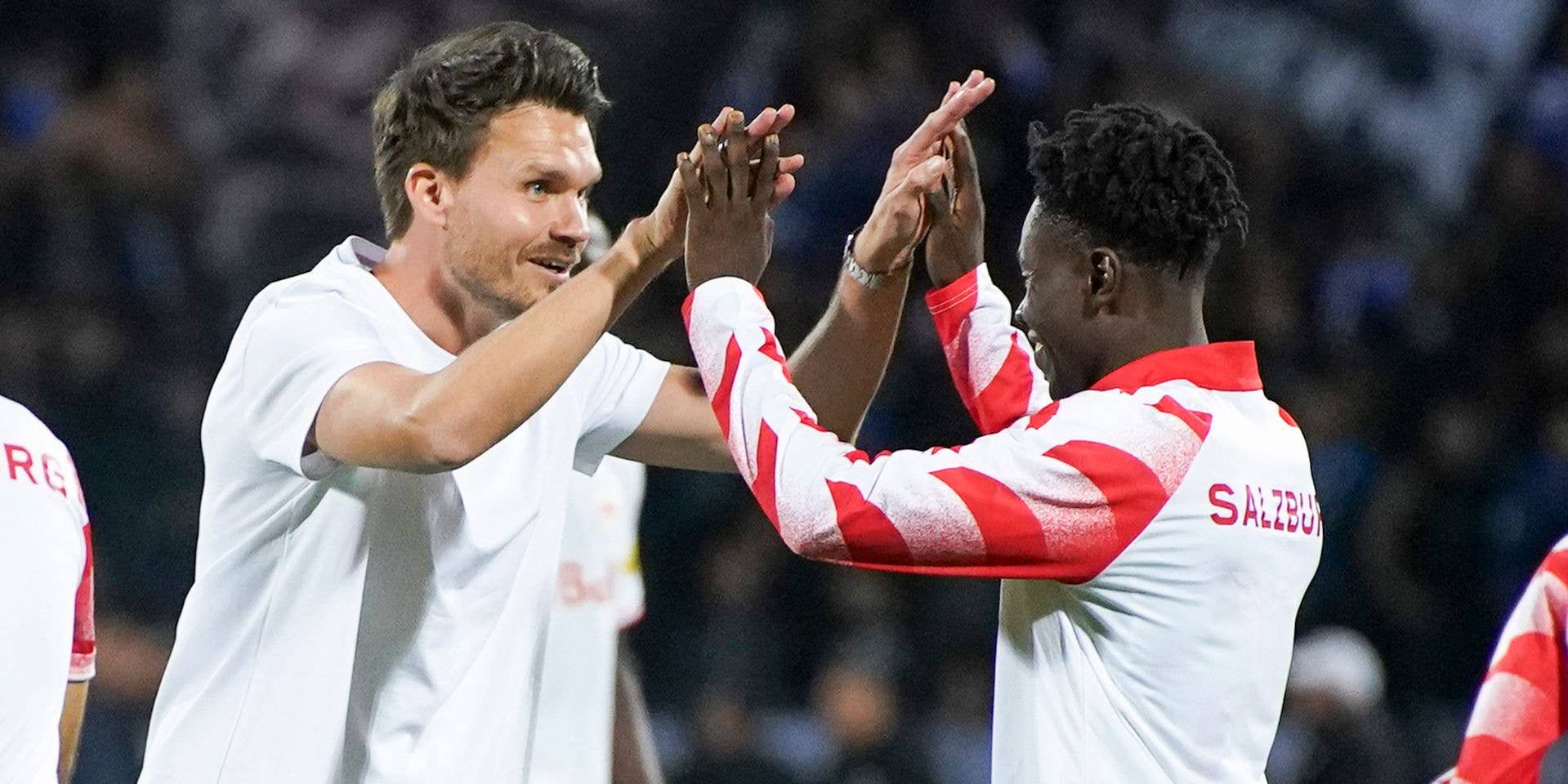 Danny Röhl und ein Spieler des FC Salzburg klatschen mit beiden Händen lächelnd auf dem Spielfeld ab.