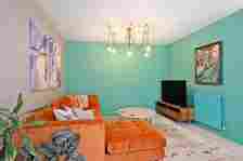 The living area in the Ferryhill home with a bright orange sofa, a statement ceiling light, turquoise walls and a flat screen television