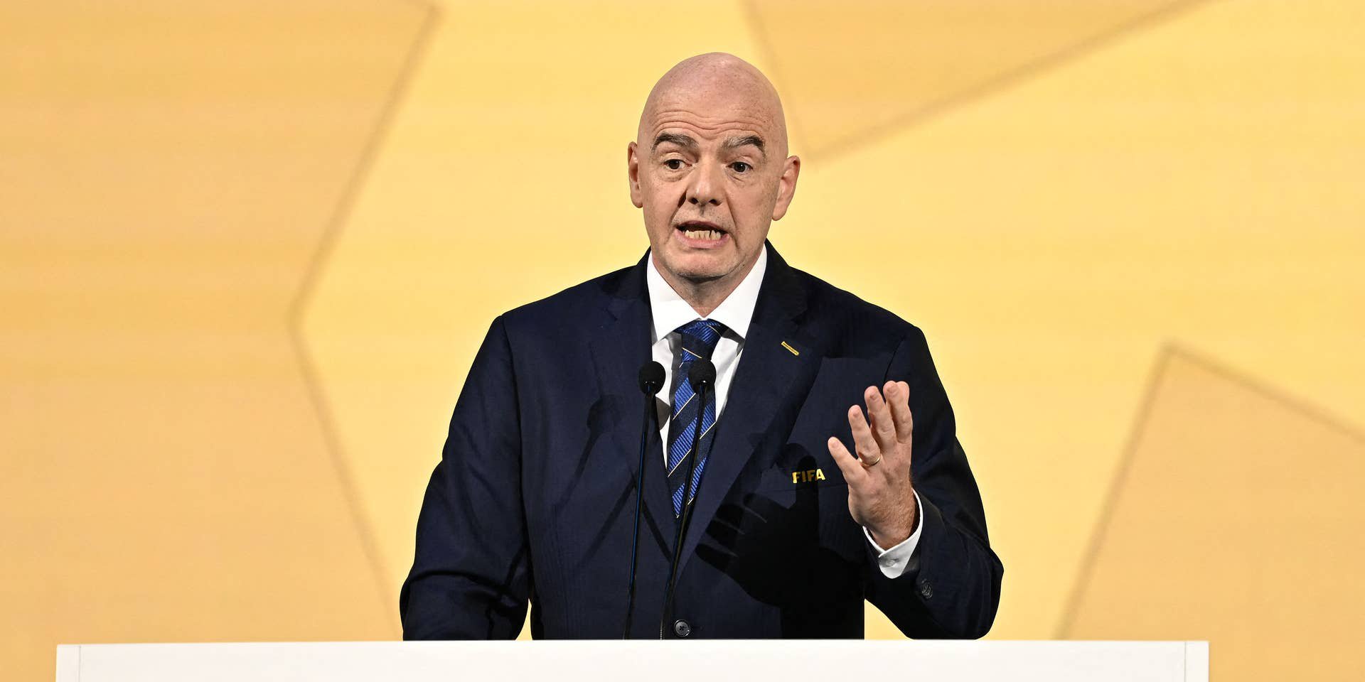 Ein Mann im Anzug spricht bei einem FIFA-Kongress an einem Podium mit FIFA-Logo.