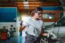 A young woman mechanic checks the oil of a car in a garage. Concept of equality