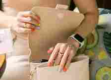 Female hands with multi-colored manicure and wrist electronic watch opening a handbag with a sexy flirting gesture. Summer mood