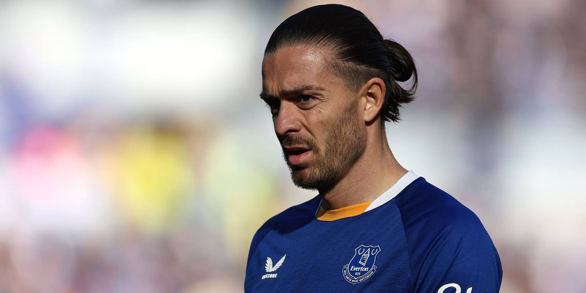 Jack Grealish blickt im blau-weißen Trikot des FC Everton mit zusammengebundenem Haar nachdenklich zur Seite.