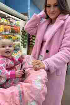 baby sits in trolley smiling while mum looks on