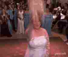 Phyllis from &quot;The Office&quot; tossing her bouquet backwards at her wedding reception as guests in formal attire watch