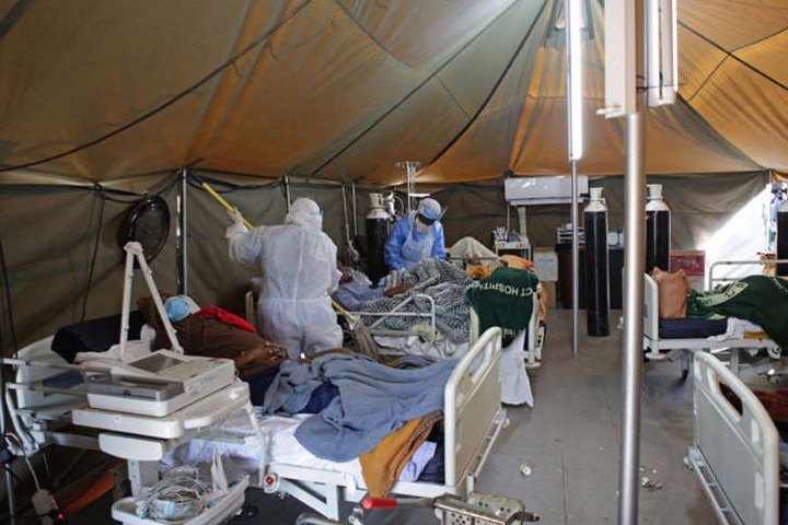 a cluttered room: FILE: A professional healthcare worker wearing personal protective equipment (PPE) treats a patient in a tent dedicated to the treatment of possible COVID-19 coronavirus patients, while another cleans the ward at the Tshwane District Hospital in Pretoria on 10 July 2020.