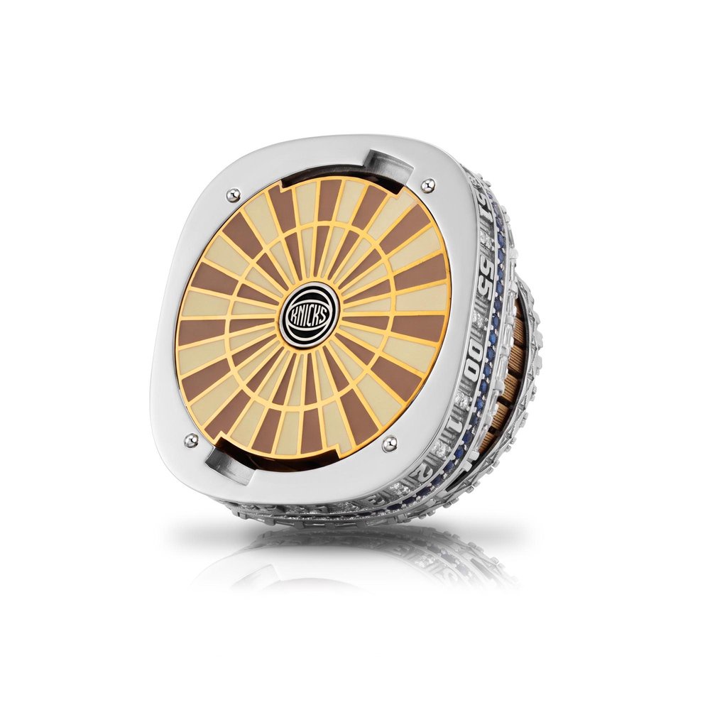 A detailed view of a Knicks NBA championship ring, featuring a parquet floor design on the face with the team logo in the center.