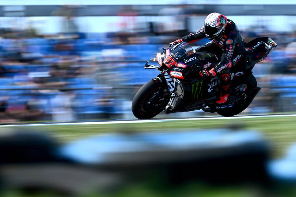 Rider in black and red leathers on a Aprilia MotoGP bike with Monster livery, leaning into a corner on track at the Australian GP