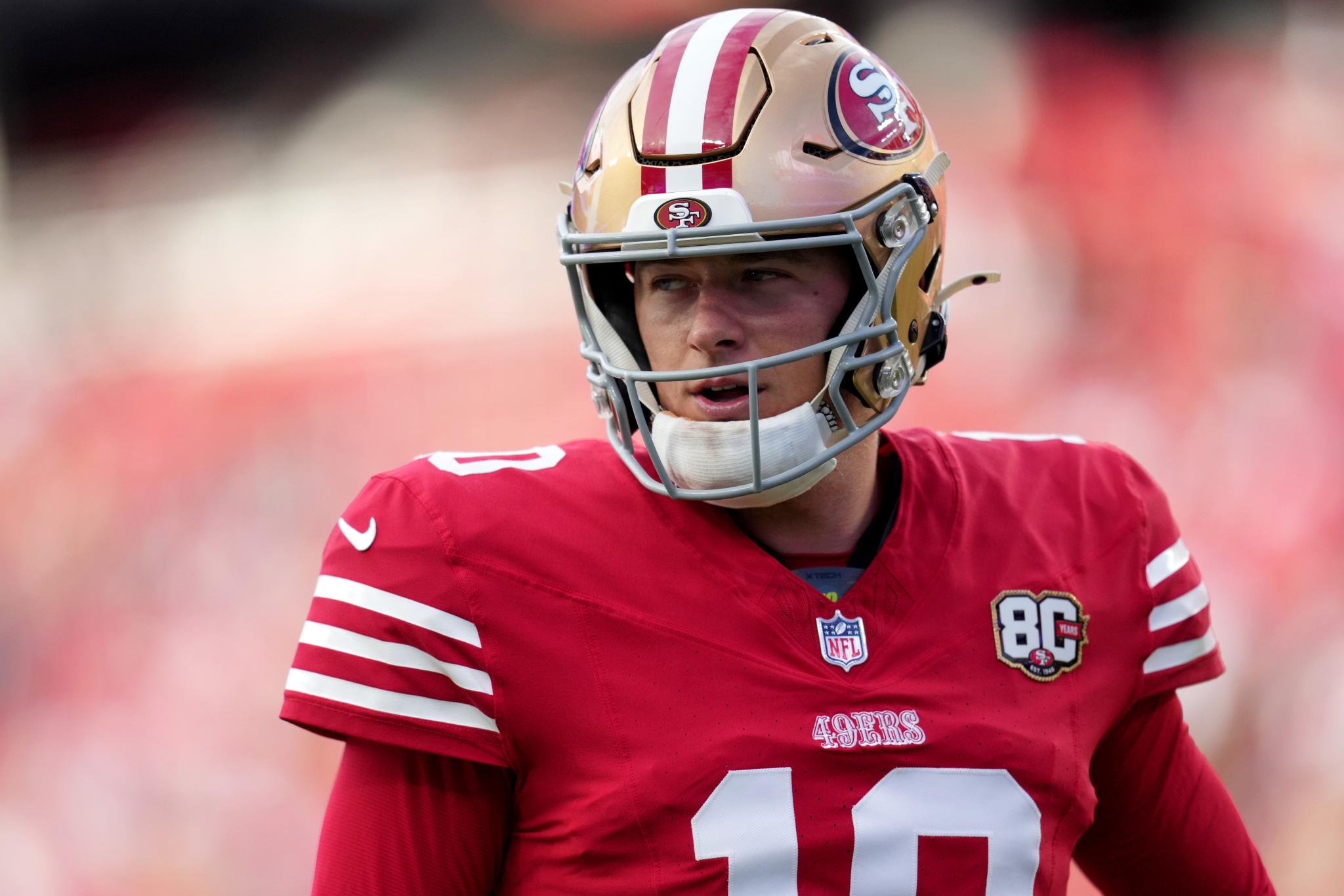 San Francisco 49ers quarterback wearing a red jersey and a gold helmet.
