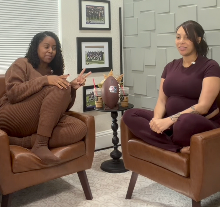Two women sitting in brown leather armchairs, with a small table between them holding a football.