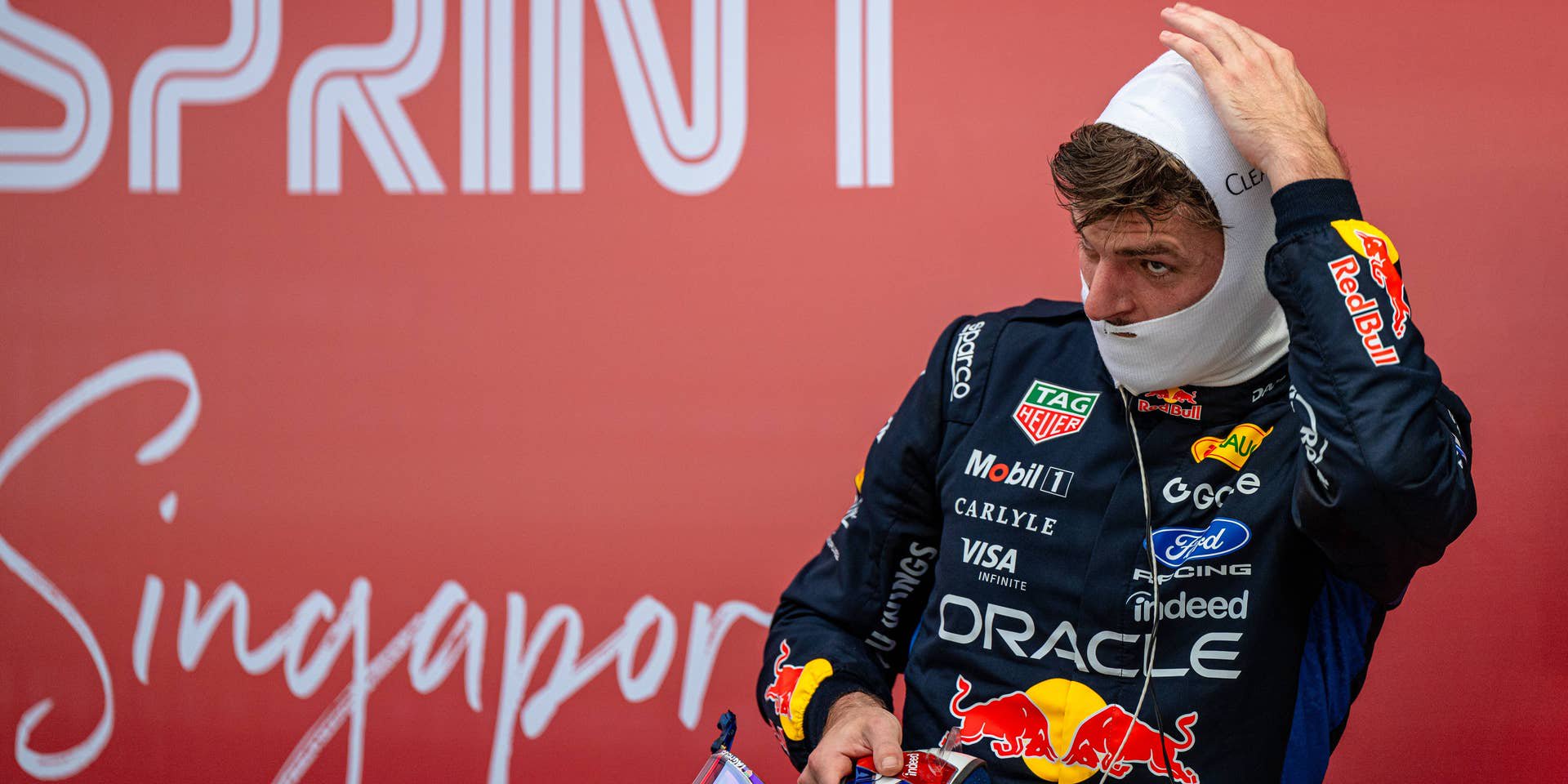 Formel-1-Fahrer im Red-Bull-Rennanzug setzt die Sturmhaube vor einem roten "Sprint"-Plakat auf.