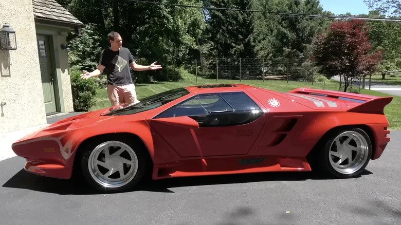 Daddy Doug DeMuro standing behind a red Wector V8 supercar.