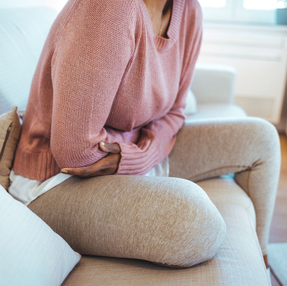 cropped shot of a woman on sofa holding stomach in pain