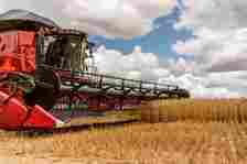 A red combine harvester operates in a wheat field under a partly cloudy sky