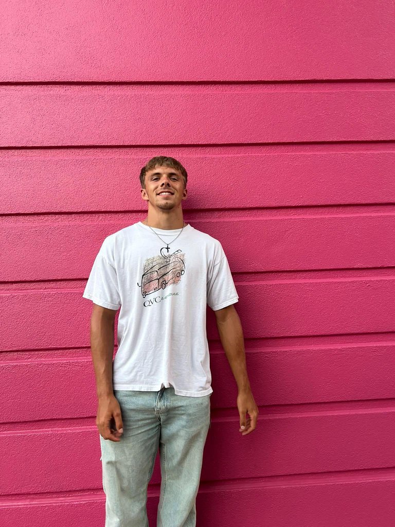 Tyler Ulrich standing in front of a bright pink wall.
