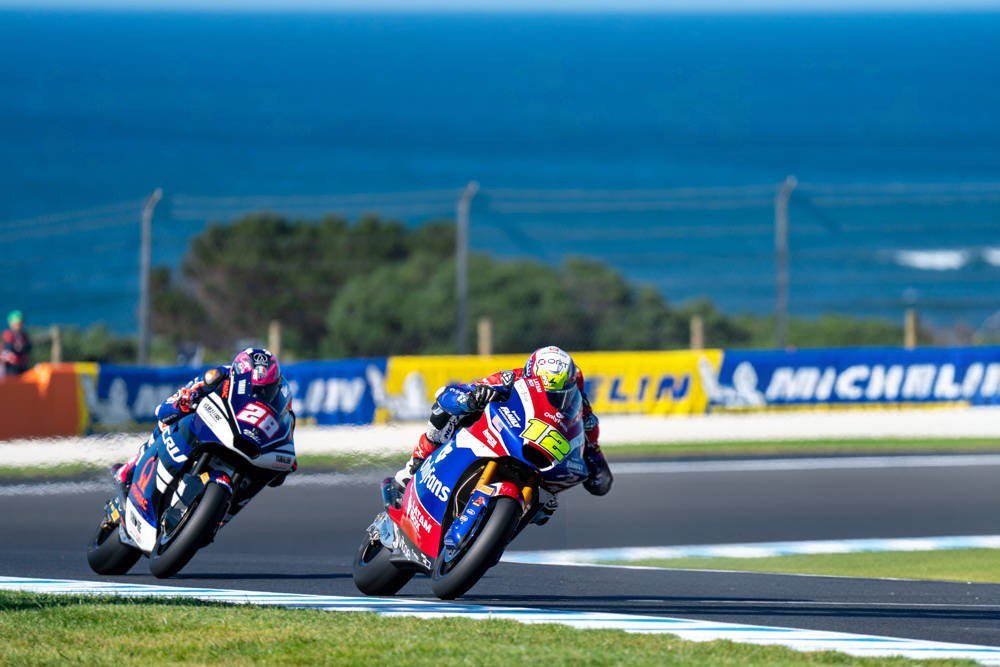 Moto2 riders battle at Phillip Island; rider in #21 leads, rider in red-white-blue #12 chases on Boscoscuro-style bike