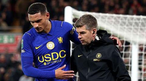 Maxence Lacroix walks off injured helped by a Chelsea physiotherapist
