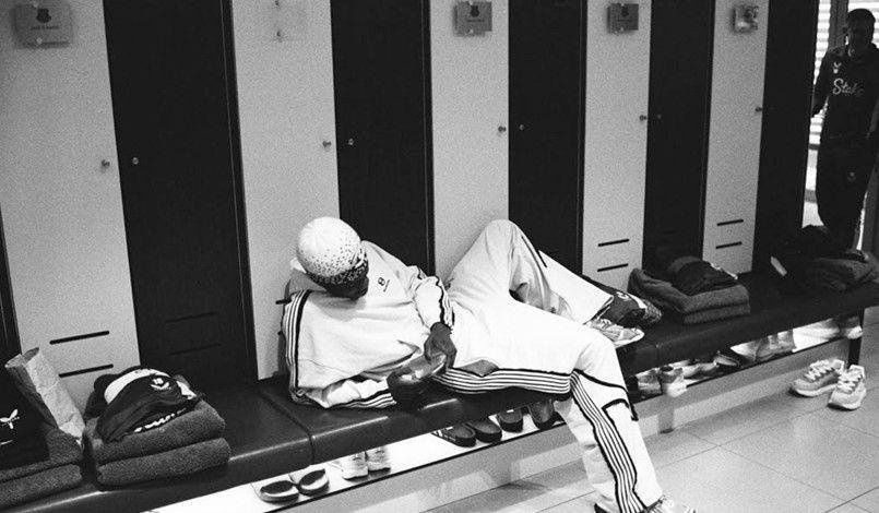 Striker Thierno Barry, who is wearing a white tracksuit, is lying down in the Everton dressing room. 
