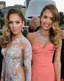 Jennifer Lopez in a white and tan floral dress next to Jessica Alba in a coral dress at the Golden Globe Awards in 2013