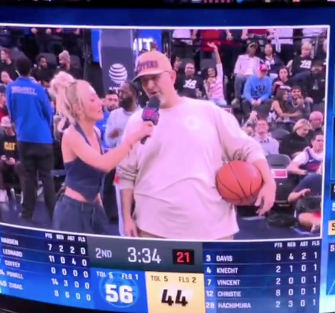 A female reporter holding a microphone and interviewing a man holding a basketball on the court.